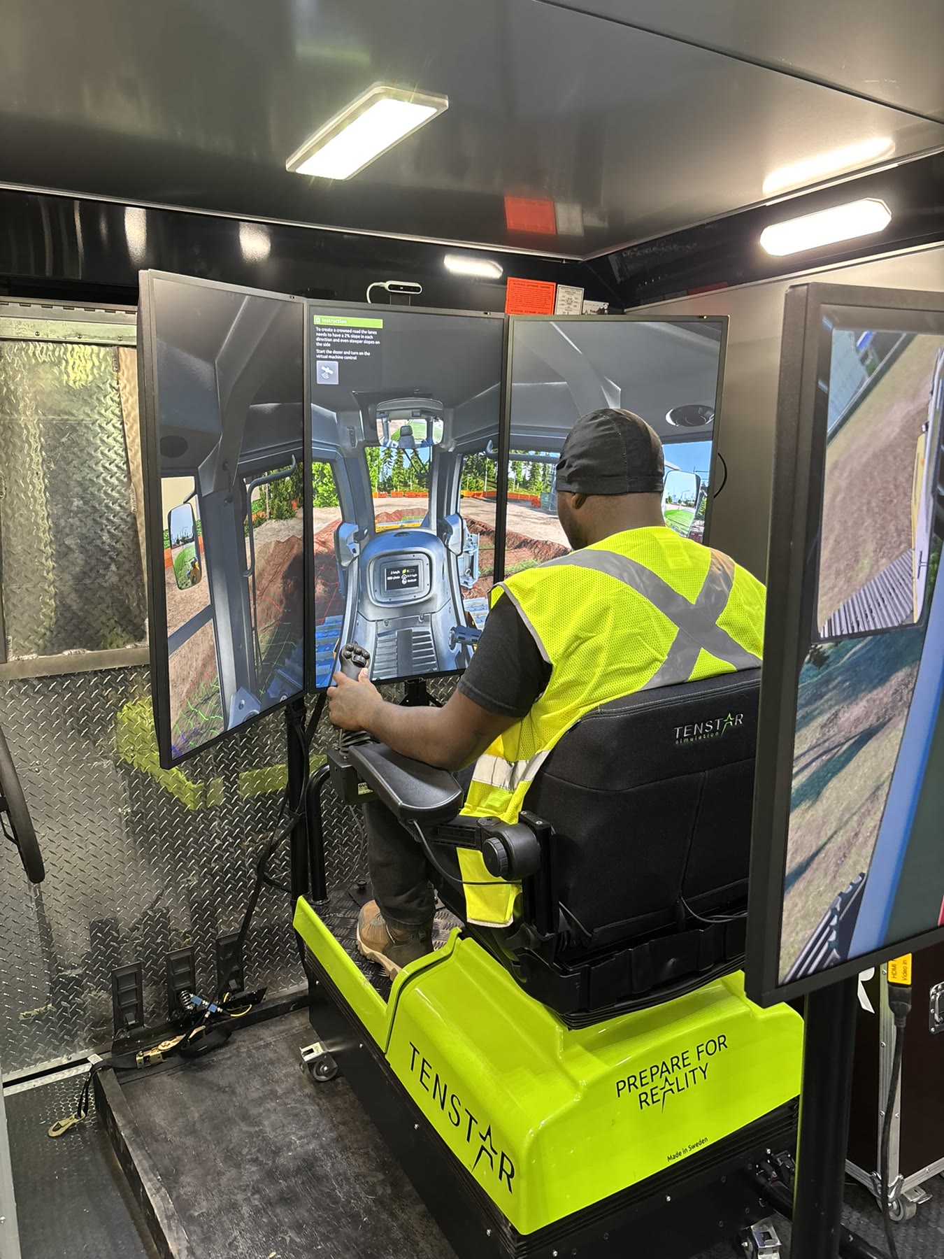 Operator practicing dozer controls on a multi-screen simulator inside the mobile unit